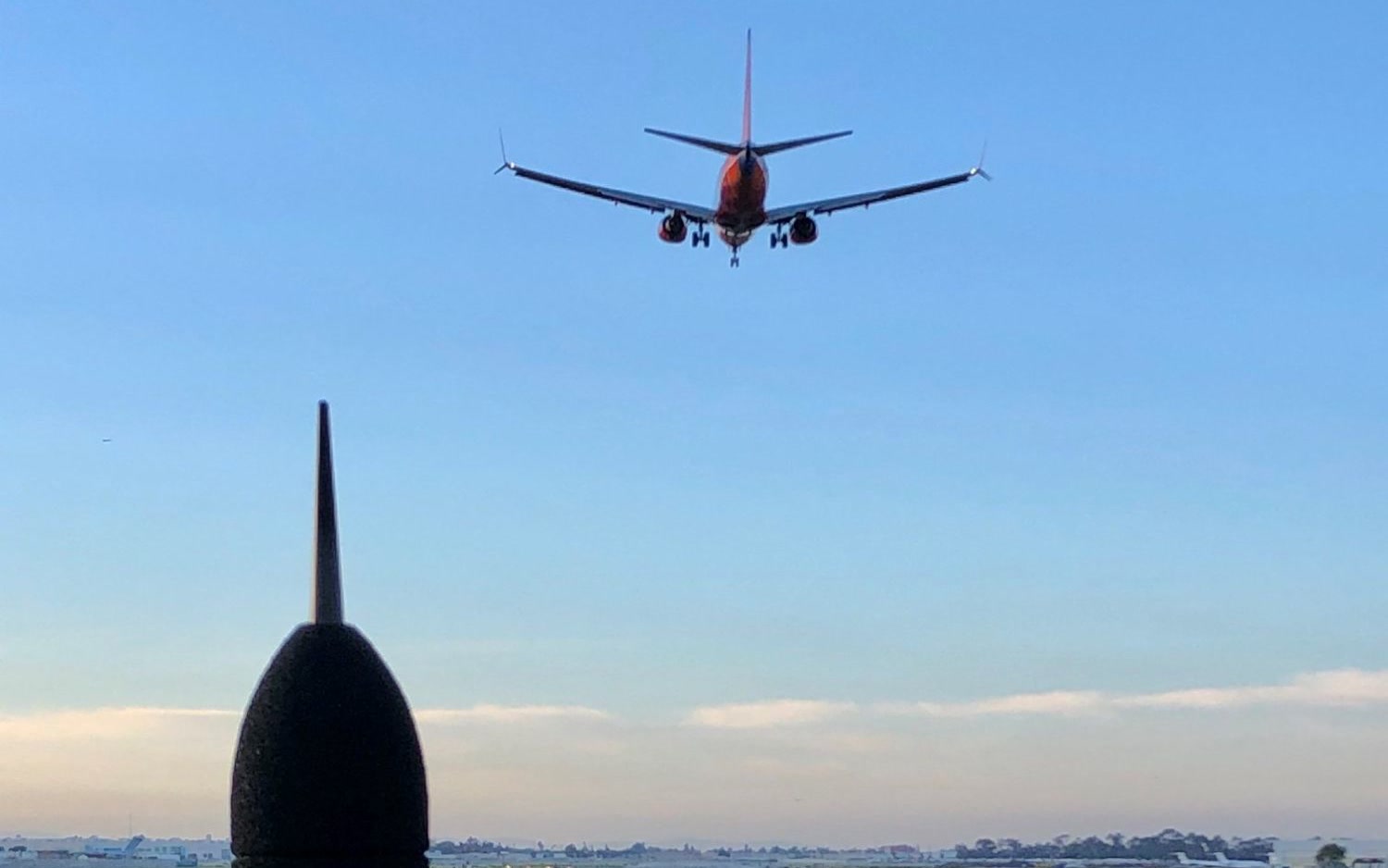 A noise monitoring microphone at the edge of an airfield as an airliner flies overhead.